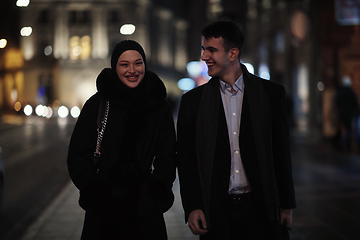 Image showing Happy multicultural business couple walking together outdoors in an urban city street at night near a jewelry shopping store window.