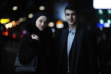 Image showing Happy multicultural business couple walking together outdoors in an urban city street at night near a jewelry shopping store window.