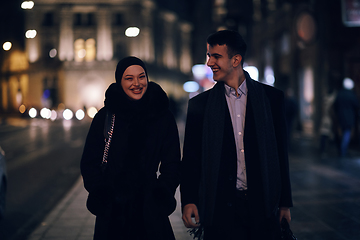 Image showing Happy multicultural business couple walking together outdoors in an urban city street at night near a jewelry shopping store window.