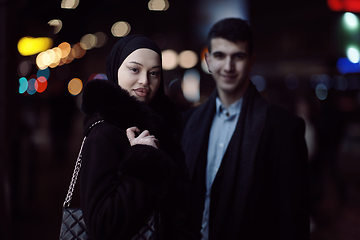 Image showing Happy multicultural business couple walking together outdoors in an urban city street at night near a jewelry shopping store window.