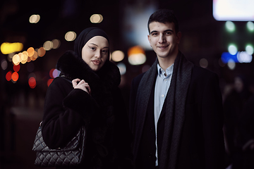 Image showing Happy multicultural business couple walking together outdoors in an urban city street at night near a jewelry shopping store window.