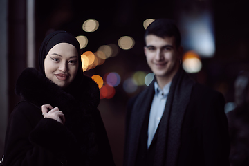 Image showing Happy multicultural business couple walking together outdoors in an urban city street at night near a jewelry shopping store window.