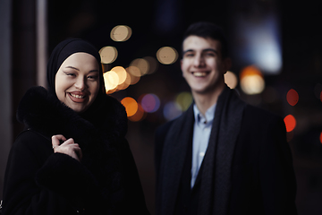 Image showing Happy multicultural business couple walking together outdoors in an urban city street at night near a jewelry shopping store window.