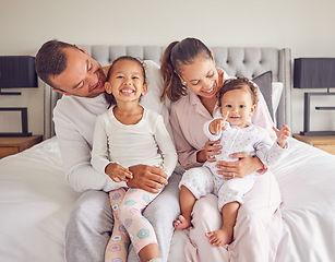 Image showing Happy, smiling and a family in pajamas on bed with small girls. Young mother and father with girl children in bedroom in the morning. Love, smile and parents with kids spending time together at home