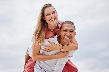 Image showing Love, couple and diversity with a happy couple outside on a cloudy day with the sky in the background. Portrait of a young man carrying a woman on his back for a piggyback ride with a smile outdoors