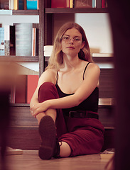 Image showing Woman, gen z and library shelf with a college student relax on a study hall or room floor. Portrait of a person with books in an education, knowledge and university center looking calm and casual