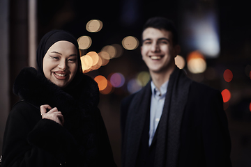 Image showing Happy multicultural business couple walking together outdoors in an urban city street at night near a jewelry shopping store window.