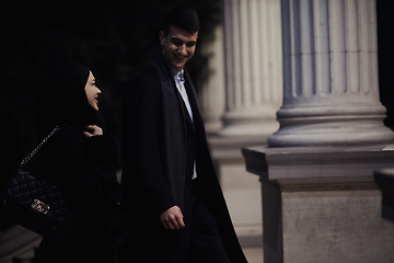 Image showing Happy multicultural business couple walking together outdoors in an urban city street at night near a jewelry shopping store window.