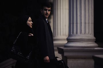 Image showing Happy multicultural business couple walking together outdoors in an urban city street at night near a jewelry shopping store window.