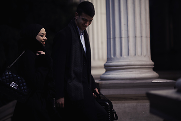 Image showing Happy multicultural business couple walking together outdoors in an urban city street at night near a jewelry shopping store window.