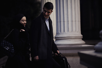 Image showing Happy multicultural business couple walking together outdoors in an urban city street at night near a jewelry shopping store window.