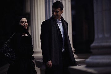 Image showing Happy multicultural business couple walking together outdoors in an urban city street at night near a jewelry shopping store window.