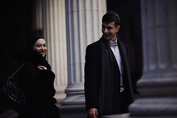 Image showing Happy multicultural business couple walking together outdoors in an urban city street at night near a jewelry shopping store window.