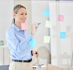 Image showing Writing, planning and thinking with sticky notes on a glass in a modern office. Happy woman manager, leader or ceo plan strategy on post it paper in a corporate marketing and advertising company