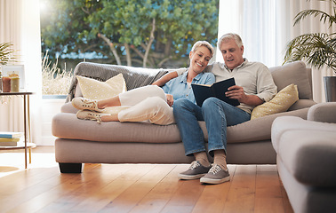 Image showing Retirement senior couple with photo album book on sofa together in summer house for vacation holiday. Happy elderly woman or people relax on couch in living room reading, talking of marriage history