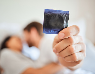 Image showing Condom, safety and safe sex with couple in bed, foreplay and intimate bonding in their home together. Passionate man showing protection in hand while kissing and being sexual with a woman in bedroom