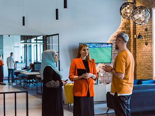 Image showing A group of young business colleagues, including a woman in a hijab, stands united in the modern corridor of a spacious startup coworking center, representing diversity and collaborative spirit