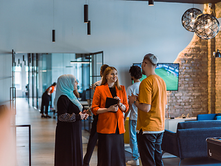 Image showing A group of young business colleagues, including a woman in a hijab, stands united in the modern corridor of a spacious startup coworking center, representing diversity and collaborative spirit