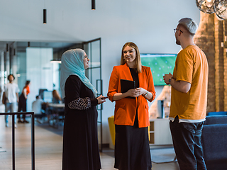 Image showing A group of young business colleagues, including a woman in a hijab, stands united in the modern corridor of a spacious startup coworking center, representing diversity and collaborative spirit