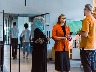 Image showing A group of young business colleagues, including a woman in a hijab, stands united in the modern corridor of a spacious startup coworking center, representing diversity and collaborative spirit