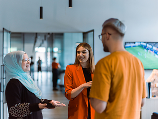 Image showing A group of young business colleagues, including a woman in a hijab, stands united in the modern corridor of a spacious startup coworking center, representing diversity and collaborative spirit