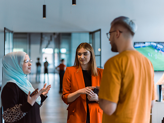 Image showing A group of young business colleagues, including a woman in a hijab, stands united in the modern corridor of a spacious startup coworking center, representing diversity and collaborative spirit