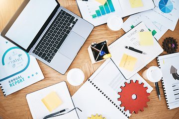 Image showing Documents, finance and report with a laptop, gear and paperwork on a table or desk in a corporate office from above. Notepad, stationery and graphs on a wooden surface in a workplace for planning