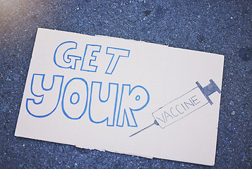 Image showing Covid, vaccine and poster with a sign on the ground outside during the corona virus pandemic. Propaganda, motivation and advertising with writing on a board for vaccination, healthcare and medicine