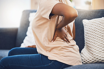 Image showing Woman with a back injury, pain or accident from stress sitting on sofa in her living room. Black girl with a muscle sprain, back pain or injured spine medical emergency on couch in lounge at home.