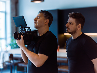 Image showing Director of photography with a camera in his hands on the set. Professional videographer at work on filming a movie, commercial or TV series. Filming process indoors, studio