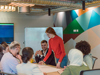 Image showing A diverse team of business experts in a modern glass office, attentively listening to a colleague's presentation, fostering collaboration and innovation