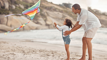 Image showing Father teaching child to fly a kite on beach wind with support, love and care. Helping, learning and fun outdoor with dad and girl kid together on holiday or summer vacation by ocean water and sand