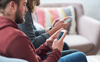 Image showing Young man using smartphone browsing social media texting messages sitting on sofa with friend