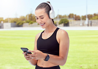 Image showing Woman athlete with phone, happy and smile with headphones and listening to music and reading a text message in the city. Young female enjoy a break from exercising outdoor and streaming audio or meme