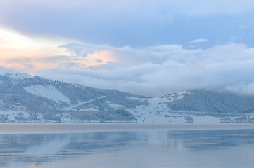 Image showing Serene Winter Sunset Over a Snow-Covered Fjord With Fog Rising