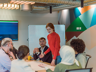 Image showing A diverse team of business experts in a modern glass office, attentively listening to a colleague's presentation, fostering collaboration and innovation