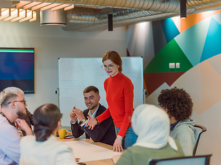 Image showing A diverse team of business experts in a modern glass office, attentively listening to a colleague's presentation, fostering collaboration and innovation