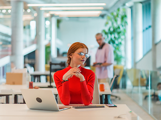 Image showing In a modern startup office, a professional businesswoman with orange hair sitting at her laptop, epitomizing innovation and productivity in her contemporary workspace