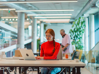 Image showing In a modern startup office, a professional businesswoman with orange hair sitting at her laptop, epitomizing innovation and productivity in her contemporary workspace