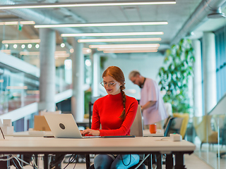 Image showing In a modern startup office, a professional businesswoman with orange hair sitting at her laptop, epitomizing innovation and productivity in her contemporary workspace