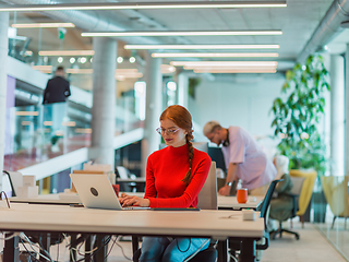 Image showing In a modern startup office, a professional businesswoman with orange hair sitting at her laptop, epitomizing innovation and productivity in her contemporary workspace