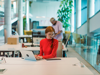 Image showing In a modern startup office, a professional businesswoman with orange hair sitting at her laptop, epitomizing innovation and productivity in her contemporary workspace