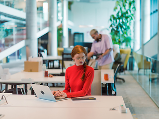 Image showing In a modern startup office, a professional businesswoman with orange hair sitting at her laptop, epitomizing innovation and productivity in her contemporary workspace