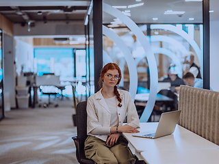 Image showing A young businesswoman with orange hair sitting confidently, fully engaged in her work on the laptop, exuding creativity, ambition, and a vibrant sense of individuality