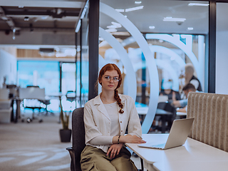 Image showing A young businesswoman with orange hair sitting confidently, fully engaged in her work on the laptop, exuding creativity, ambition, and a vibrant sense of individuality