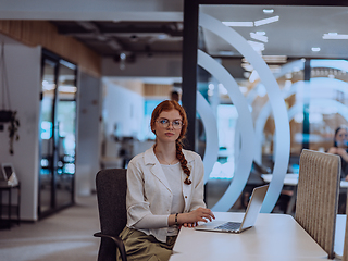 Image showing A young businesswoman with orange hair sitting confidently, fully engaged in her work on the laptop, exuding creativity, ambition, and a vibrant sense of individuality