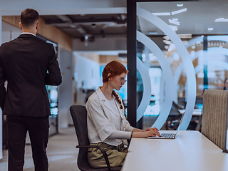 Image showing A young businesswoman with orange hair sitting confidently, fully engaged in her work on the laptop, exuding creativity, ambition, and a vibrant sense of individuality