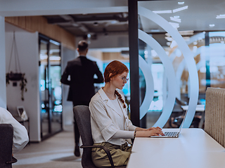 Image showing A young businesswoman with orange hair sitting confidently, fully engaged in her work on the laptop, exuding creativity, ambition, and a vibrant sense of individuality