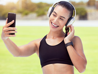 Image showing Phone, woman and fitness influencer taking a selfie at training, running and workout outdoors on sports racetrack. Smile, healthy and happy girl in headphones sharing fitness journey on social media