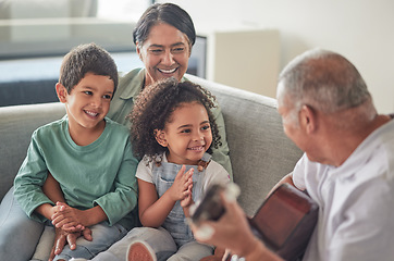 Image showing Grandfather playing the guitar for grandmother and children sitting on the sofa in their home. Retired grandparents entertain happy and smiling grandchildren with music on acoustic guitar and bonding